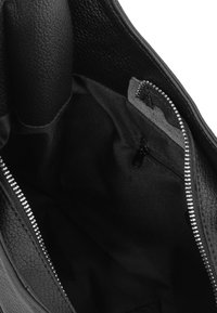 Juodas odinis kuprinės vidus, pasižymintis tekstūruota paviršiumi, dideliu pagrindiniu skyriumi ir užtrauktuku su sidabro spalvos užtrauktuku.