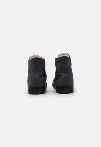 Adidași negri înalți din pânză, cu tălpi din cauciuc și un finisaj texturat, având un patch logo circular pe laterale și un design clasic.