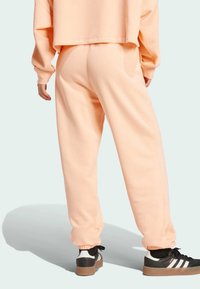 Svetloružové tepláky vyrobené z mäkkej tkaniny, s elastickými manžetami a vo voľnom strihu, v kombinácii s čierno-bielymi teniskami.