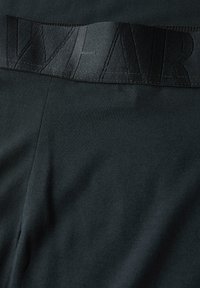 Tmavě šedá tkanina s hladkým povrchem, která má široký černý pás s embosovanými písmeny tvořícími slovo "WEAR." Zaměření na jednoduchost a pohodlí.