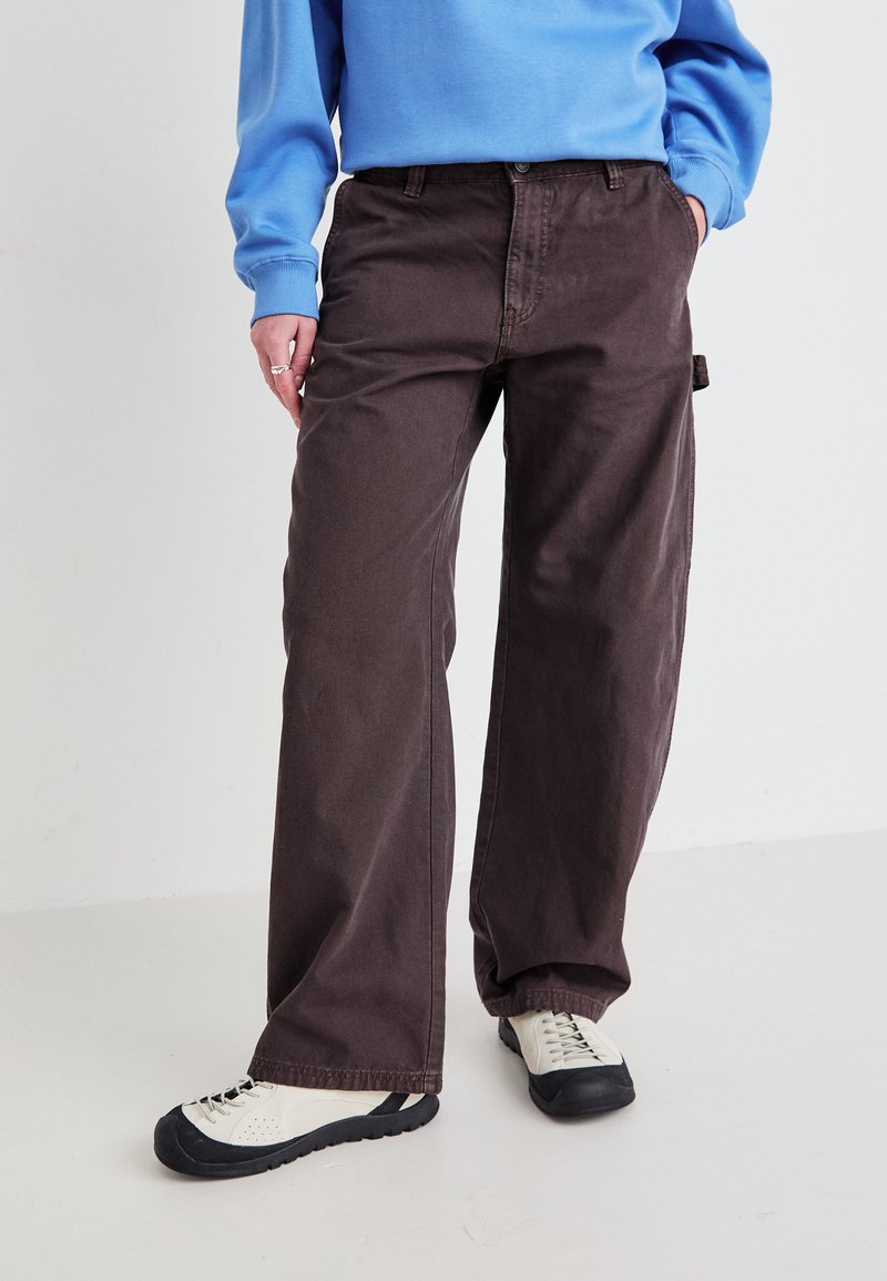 Brune vide bukser laget av mykt stoff, med knappelukking og en sidelomme. Kombinert med lyse sneakers.