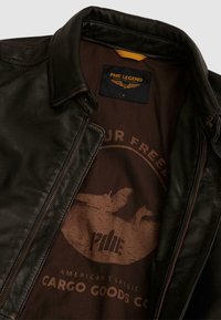Schwarze Lederjacke mit braunem Innenfutter, das eine runde Grafik und den Text "PME Legend American Classic Cargo Goods Co." zeigt