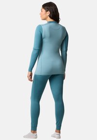 A fitted two-piece activewear set in a soft teal color, featuring long sleeves and leggings made from a smooth, stretchy fabric.