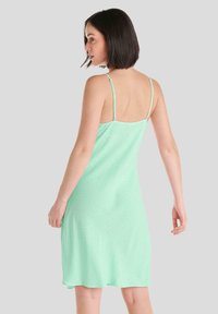 Vestido de tirantes finos en verde menta claro, con una textura suave y un diseño sutilmente patternado. La vista trasera muestra un corte relajado y hasta la rodilla.