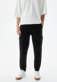 Zwarte cargobroek met voor- en zijzakken, smal toelopende pasvorm, gemaakt van katoen. Gecombineerd met een losse witte t-shirt en sneakers.