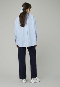 Chemise oversized rayée bleu et blanc à manches longues, portée avec un pantalon marine et des baskets blanches, avec un nœud dans les cheveux.