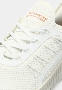 Gros plan d'une basket Skechers BOBS blanche avec tige en mesh, lacets blancs et semelle texturée.