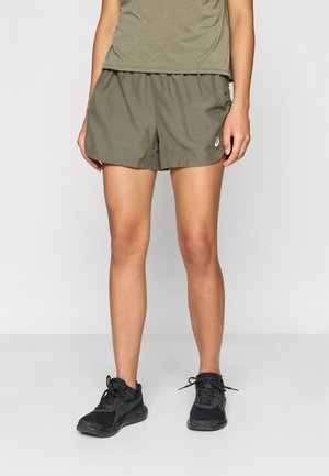 Olivengrønne træningsshorts i let materiale, med elastisk talje og subtil tekstur. Kombineret med sorte løbesko.