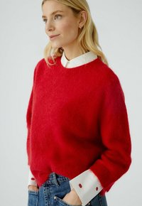 Roter flauschiger Pullover aus weichem Material, kombiniert mit einem weißen Hemd, das rote Kussakzente an den Manschetten aufweist. Lässige Passform und strukturierter Design.