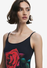 Fekete izzadságszívó trikó, melynek elülső részén egy nagy, élénk piros rózsa grafika és zöld levelek találhatók. Vékony vállpántokkal és sima szövet textúrával rendelkezik.