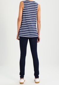 Marinblå och vit randig ärmlös topp i kombination med mörkblå skinny jeans och vita skor, sedd bakifrån.