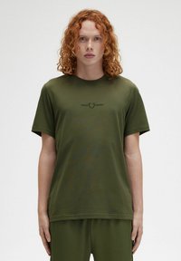 Camiseta de algodón verde oliva de manga corta, con un sutil logo negro en el pecho. Textura suave y corte relajado.