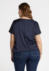 Top in raso navy con maniche corte, vestibilità rilassata, scollatura rotonda e delicato dettaglio della cucitura sul retro, abbinato a jeans in denim scuri.