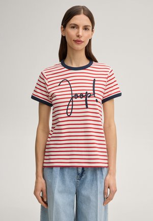 Femme aux cheveux bruns raides portant un t-shirt blanc à rayures rouges avec bordure marine et texte brodé "Joop!" en bleu, associé à un jean bleu clair.