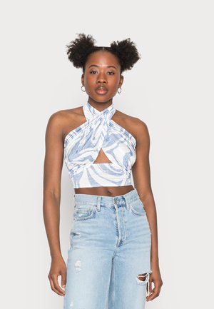 Top halter azul e branco com padrão, com alças cruzadas e um recorte frontal, combinado com jeans de cintura alta desbotados em azul claro.