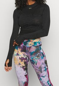 Svart långärmad träningsöverdel med texturerad design och tumhål, i kombination med färgglada leggings med abstrakt mönster och lila detaljer.