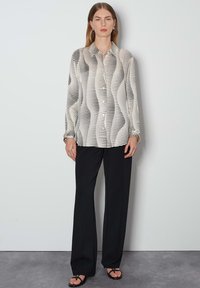 Long-sleeve blouse in cream and black with wavy stripe pattern, button-up front, and gathered cuffs, paired with black trousers and sandals.