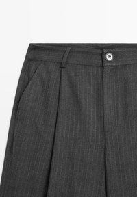 Pantalon gris foncé à fines rayures, avec plis à l'avant, poches latérales, passants de ceinture et une fermeture à bouton unique à la taille.