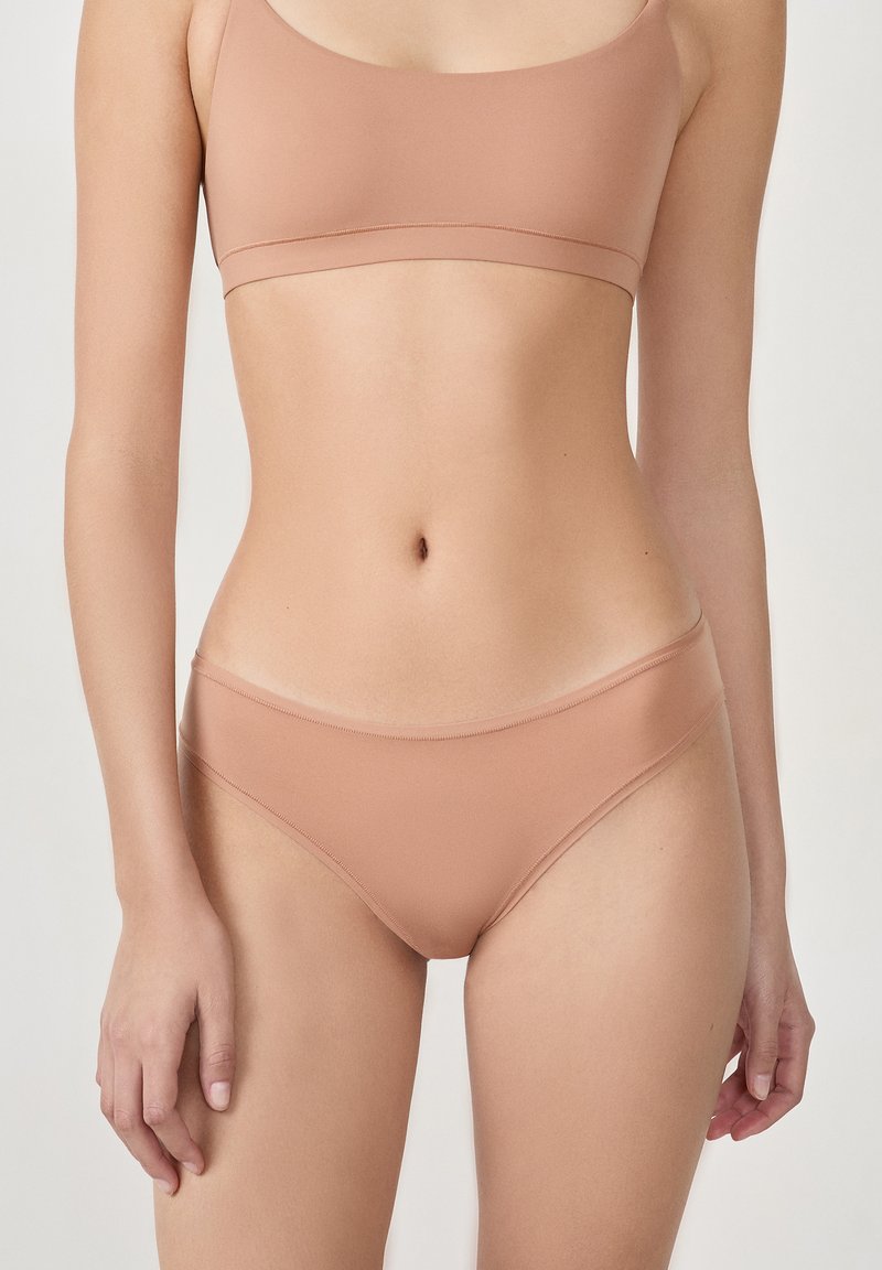 Beiges nahtloses Bralette und passendes Bikini-Unterwäsche-Set aus einem glatten, dehnbaren Material. Verfügt über ein minimalistisches Design mit dünnen Trägern.