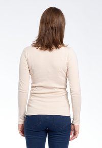 Maglia a maniche lunghe beige realizzata in tessuto morbido, con una forma aderente e una texture liscia, abbinata a jeans blu scuro con un classico design a cinque tasche.