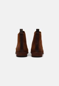 Bottines en suede marron avec un dos en cuir lisse, une petite languette de tirage et un talon en bois empilé, présentant un design minimaliste.