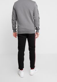 Grå sweatshirt med texturerade ärmar, i kombination med svarta sweatpants med röda sidostreck. Vita sneakers fulländar looken.