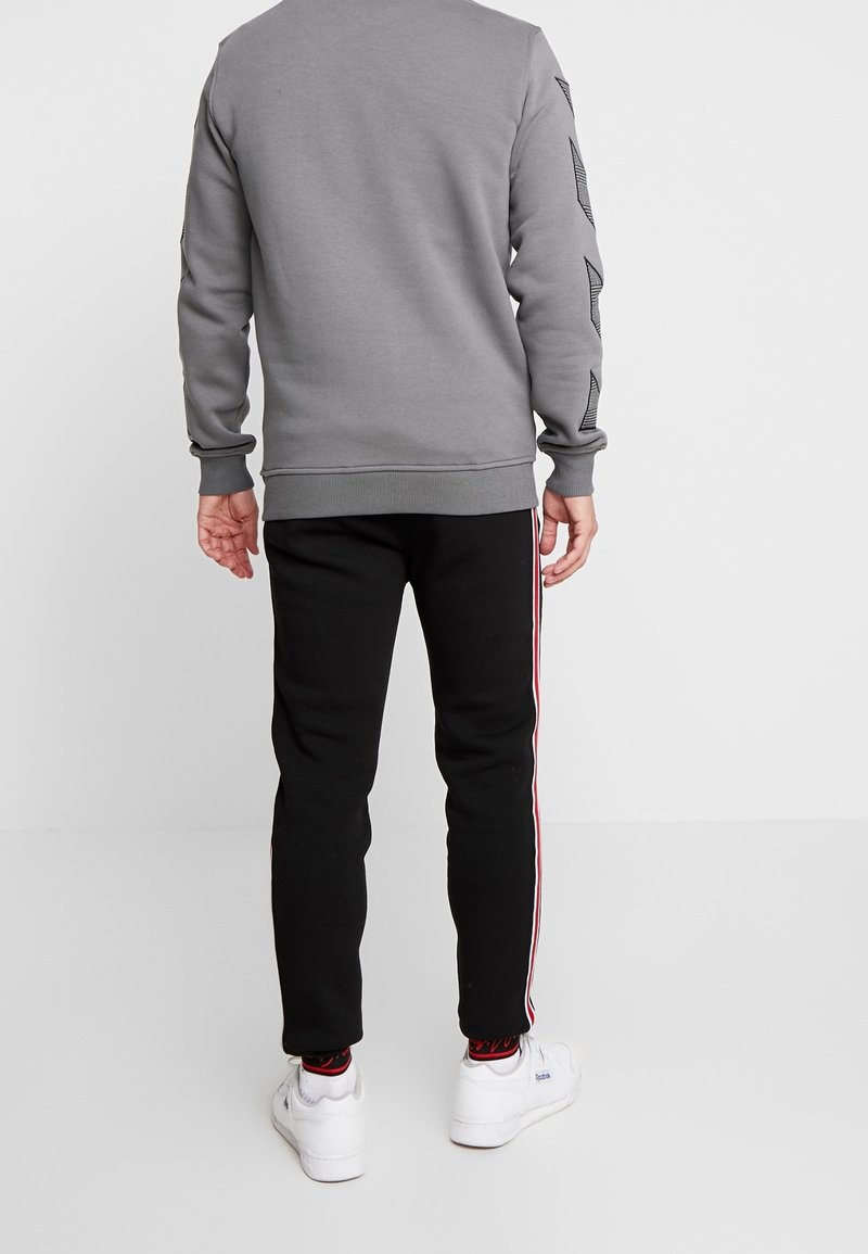 Grå sweatshirt med texturerade ärmar, i kombination med svarta sweatpants med röda sidostreck. Vita sneakers fulländar looken.