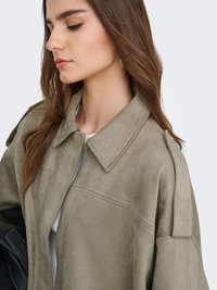Olivengrønn jakke i kunstig semsket skinn med stor krage, glidelås og avslappet passform. Har skulderpynt og sidelommer.