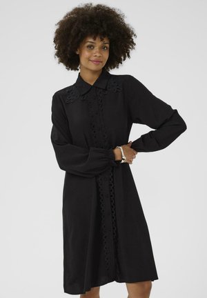 Black dress with long sleeves and a collar, featuring floral embroidery on the shoulders and circular cut-out accents down the front.