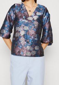 Lila und blaue Blumensatinbluse mit V-Ausschnitt und Dreiviertelärmeln, mit strukturierten metallischen Details und lockerer Passform.