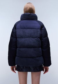 Námořnická puffer bunda s texturovaným hřejivým límcem, prošívanými částmi a volným střihem. Materiál kombinuje hladký a kordový povrch.