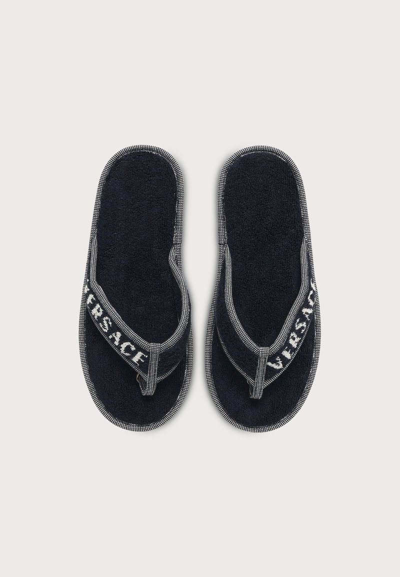 Coppia di sandali infradito in spugna nera con bordo bianco e scritta "VERSACE" sulle fascette in tessuto su sfondo bianco semplice.
