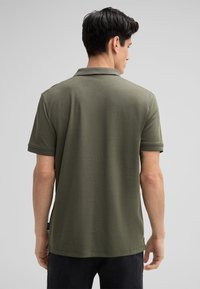 Olivgrünes Poloshirt mit kurzen Ärmeln, ausgestattet mit einem gerippten Kragen und Bündchen sowie einer glatten Textur; seitliche Schlitze am Saum für Bewegungsfreiheit.