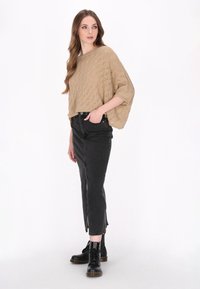 Pulover bej, tricotat, cu croială scurtă și o potrivire lejeră, având un model texturat, asortat cu blugi negri, cu talie înaltă, și cizme negre cu șireturi.