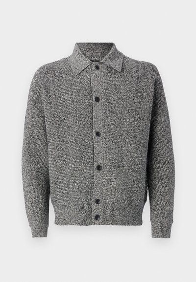 Pelēka adīta jaciņa ar apkakli, garām piedurknēm un priekšējo pogu aizdari. Ir raksturīgs teksturēts raksts un ribināta apakšmala un piedurknes.