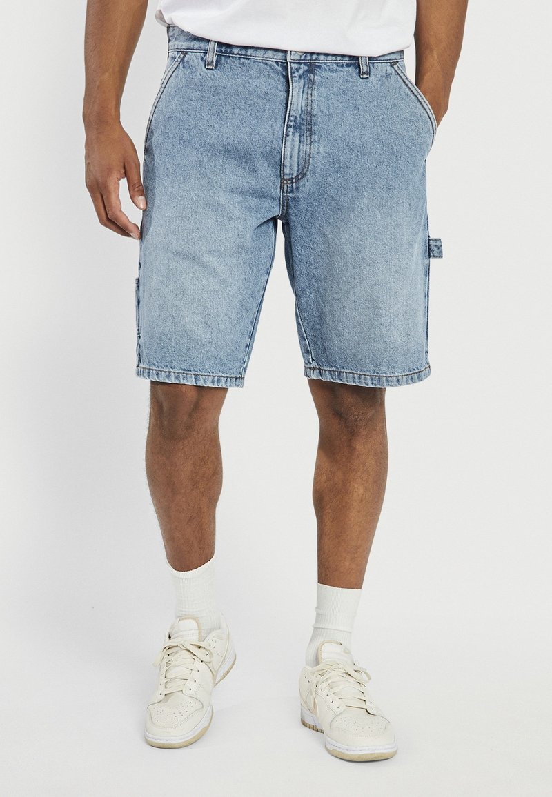 Shorts de mezclilla azul claro con un ajuste holgado, cinco bolsillos y un bolsillo lateral tipo cargo. Cuenta con un cierre de botón y cremallera.
