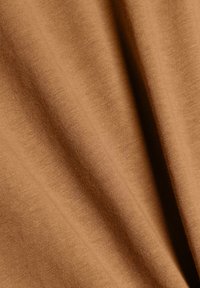 Tissu marron avec une texture tissée visible et des plis doux créant des plis ombragés.