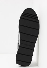 Suola di sneaker nera con scanalature orizzontali, gomma testurizzata e un branding sottile. Il lato presenta un design in rete con un motivo leggero.