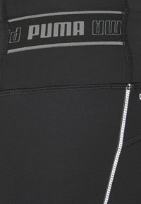 Svarta träningsleggings med en bred grå midja med "PUMA"-logotyp, platta sömmar och reflekterande detaljer längs sidan.