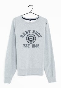 Sweatshirt gris avec un col rond, des manches raglan et des poignets côtelés. Présente un texte noir et un design de logo circulaire à l'avant.