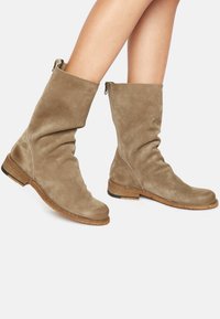 Botines de ante beige con un diseño arrugado, punta redonda y tacón bajo apilado. Detalle de cremallera en el costado para facilitar su uso.