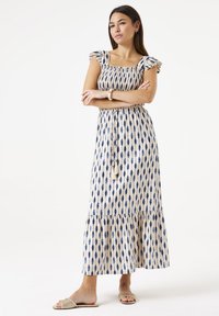 Maxikleid mit quadratischem Ausschnitt und Rüschensäumen. Hat ein blau-beiges Blattmuster, taillierte Taille und einen gestuften Saum.