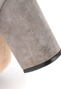 Gros plan d’un talon de chaussure en daim gris avec une semelle en caoutchouc noire sur fond blanc.