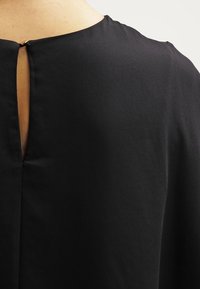 Sort beklædning med åbning i ryggen i form af en nøglehulsåbning og en glat tekstur. Har minimalistisk design og rene, lige linjer.