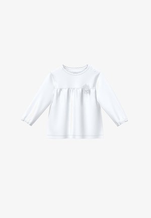 Chemise pour bébé à manches longues blanche avec col rond, deux boutons-pression aux épaules, couture froncée sur la poitrine, et petite décoration en dentelle florale sur le côté droit devant.