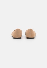 Tan suede flats with a low black heel, rounded toe, and minimal stitching detail along the back. Smooth texture with a classic silhouette.