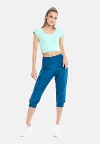 Top corto verde claro con mangas cortas, combinado con pantalones capri azules que tienen una cinturilla ancha y bolsillos laterales texturizados. Zapatillas blancas completan el atuendo.