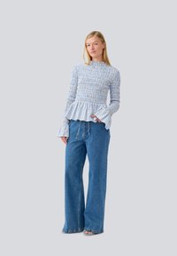 Camisa listrada azul e branca com textura franzida e mangas largas, combinada com calças de denim azul de corte solto e sandálias.