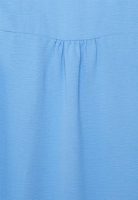 Tessuto di blusa azzurro chiaro con una texture scelto. Presenta dettagli arricciati sul collo, creando una morbida drappeggiatura.