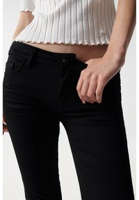 Jeans skinny negros de mezclilla, con cierre de botón, cinco bolsillos y una textura suave, combinados con una blusa blanca de canalé.